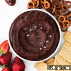 A bowl of edible cookie dough dip next to pretzels and strawberries.