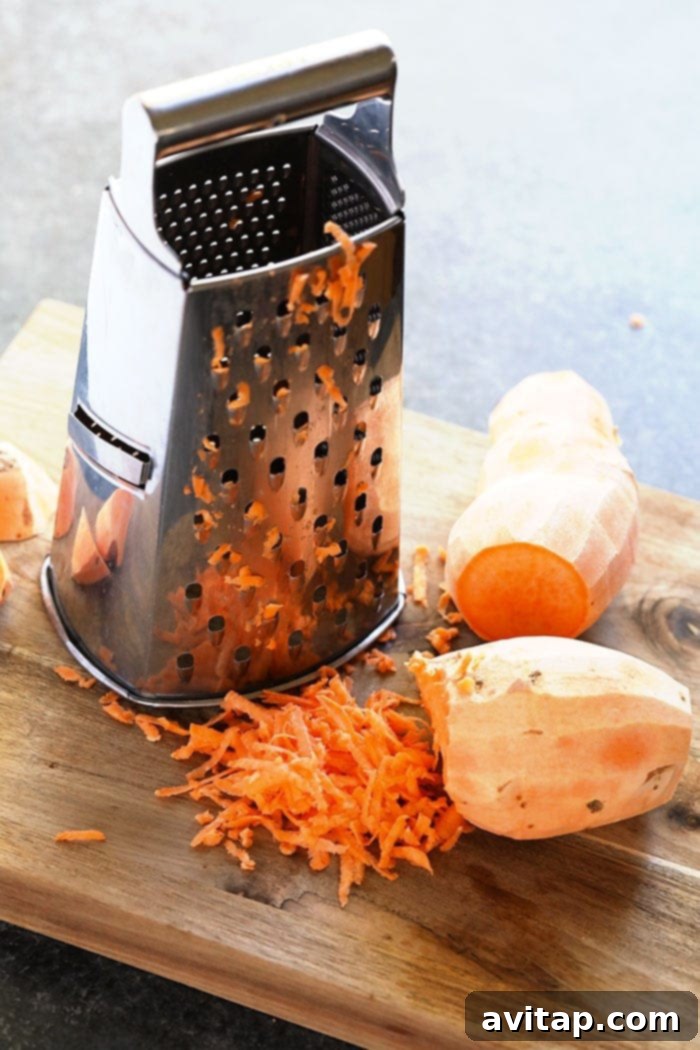 Hands grating a sweet potato with a cheese grater.