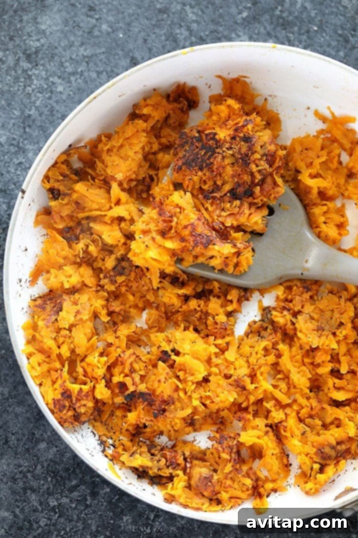 Sweet potato hash browns sizzling in a pan on the stovetop.