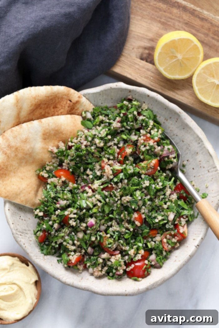 A beautifully presented bowl of Quinoa Tabouli, garnished with fresh herbs and a spoon, ready to be enjoyed.