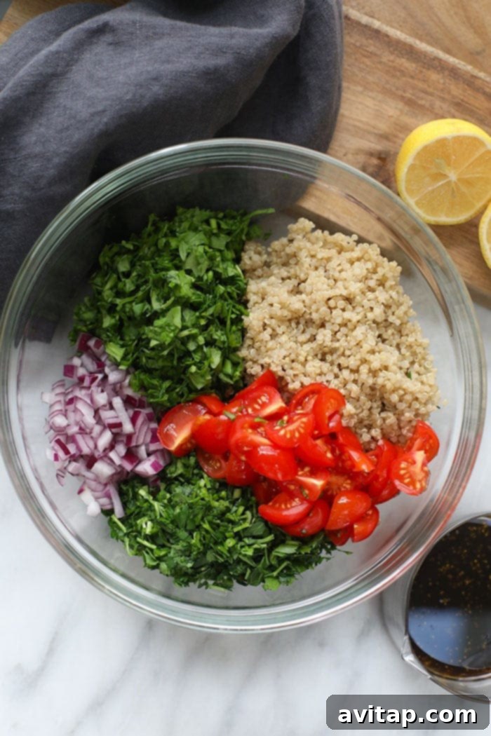 A vibrant assortment of fresh ingredients for tabouli, including parsley, tomatoes, red onion, and cooked quinoa, arranged in separate bowls.