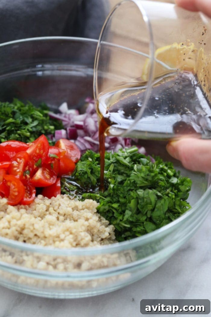 Close-up of a hand pouring a zesty dressing over the quinoa tabouli salad in a large mixing bowl, ensuring even coating.