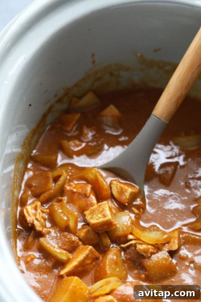 Stirring Slow Cooker Chicken Tikka Masala Slow cooker chicken tikka masala being stirred with a spoon in a crock pot.