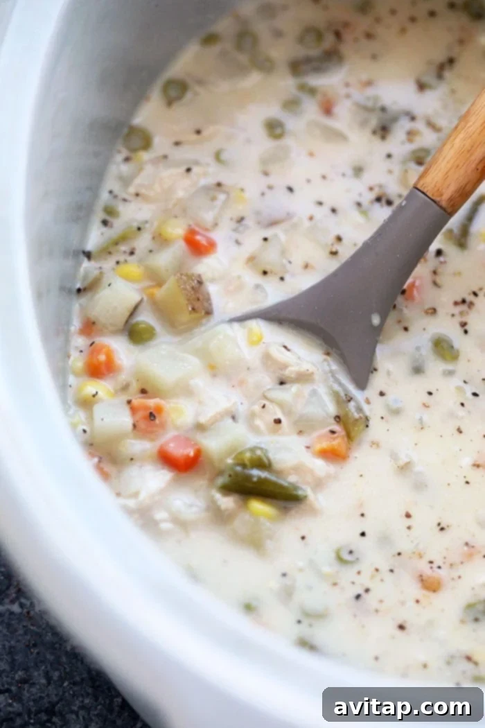 Close-up of a spoon dipping into a bowl of Slow Cooker Chicken Pot Pie Soup, showcasing its rich, creamy texture and hearty ingredients.