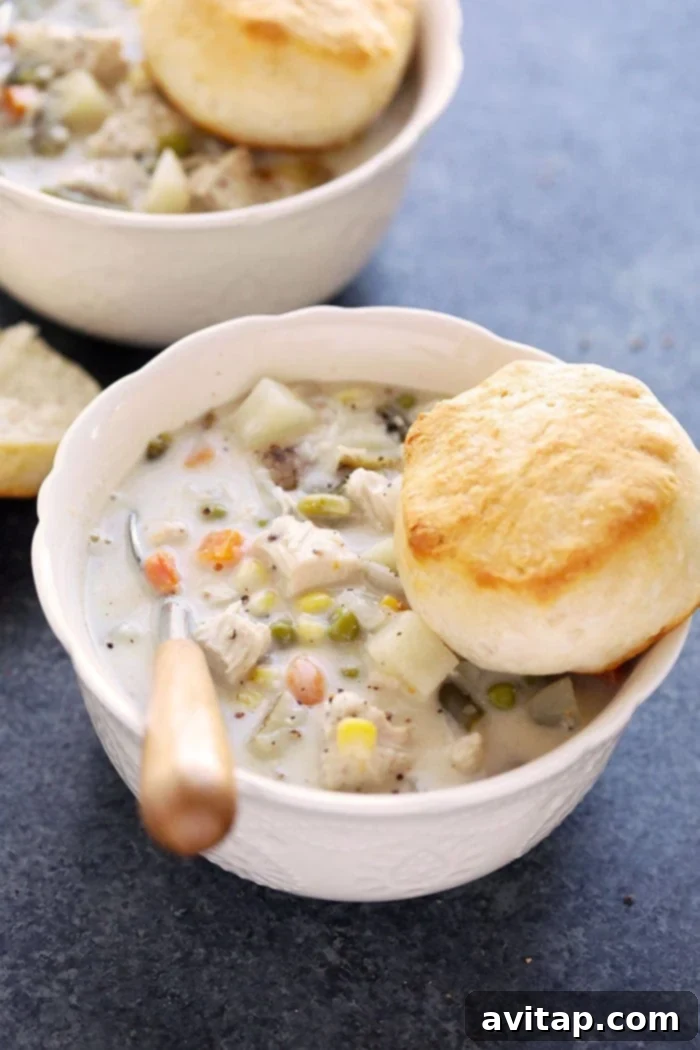 A beautifully presented bowl of Slow Cooker Chicken Pot Pie Soup, served with a golden, flaky biscuit on the side, ready to be devoured.