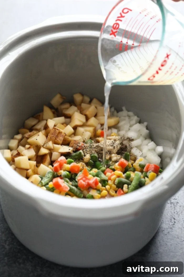 All the fresh ingredients for Slow Cooker Chicken Pot Pie Soup laid out on a wooden board: chicken, frozen vegetables, potatoes, onion, and spices.