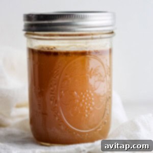 A jar of homemade chicken broth with fresh herbs.