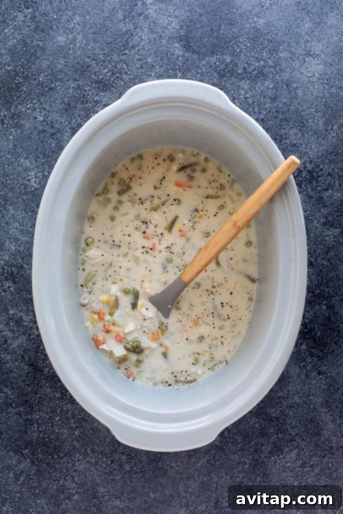 Close-up of creamy Slow Cooker Chicken Pot Pie Soup in a bowl with a spoon, highlighting its rich texture and chunks of ingredients.