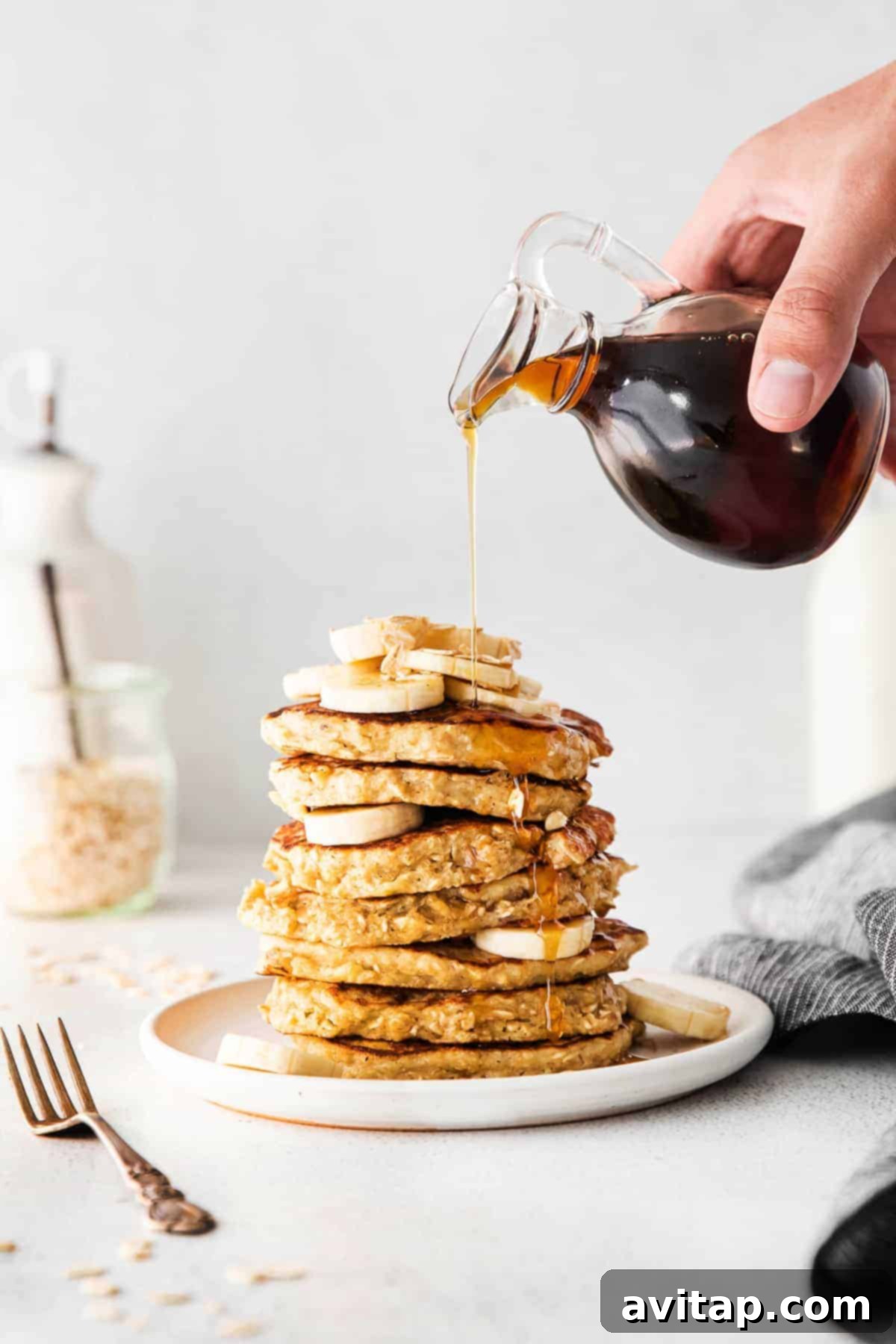 Syrup Drizzled Banana Oatmeal Pancakes A stack of golden banana oatmeal pancakes being drizzled with warm maple syrup.