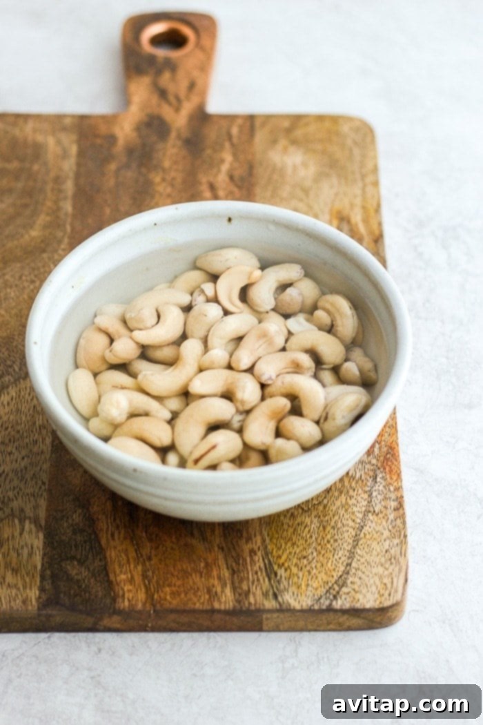 Raw cashews soaking in a bowl of water, essential for a smooth vegan cheese sauce.