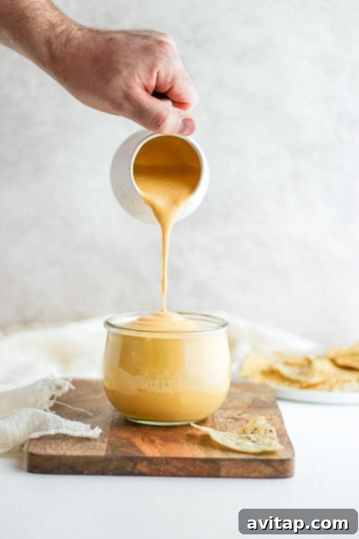 Creamy vegan cheese sauce being poured into a glass jar for storage.