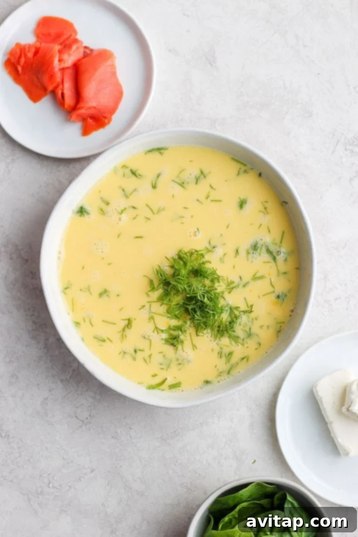 Bowl of whisked eggs with almond milk and dill, ready for frittata preparation.