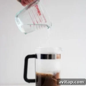 A person pouring hot water into a French press over coffee grounds.