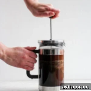 A person pressing down the plunger of a French press coffee maker.