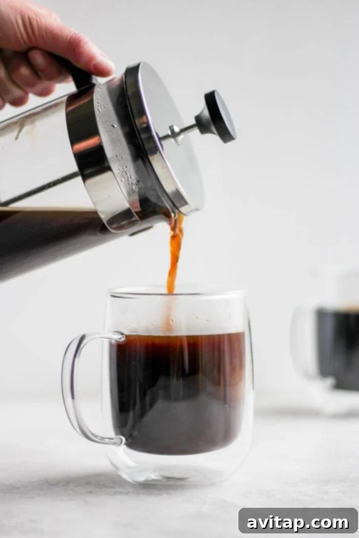 Pouring freshly brewed French press coffee into a ceramic mug.