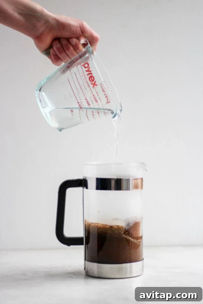 Pouring hot water into a French press over coffee grounds.