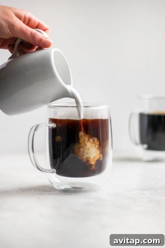 Pouring fresh cream into a cup of French press coffee.