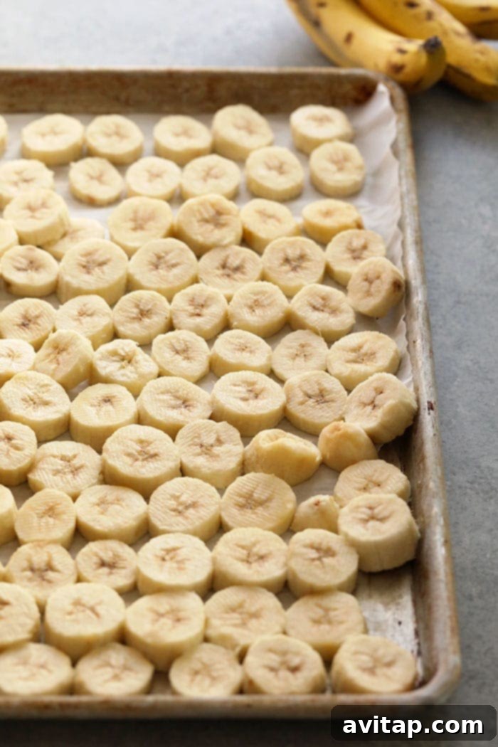 Uniform slices of ripe bananas carefully arranged in a single layer on parchment paper on a baking sheet, impeccably spaced and ready for flash freezing