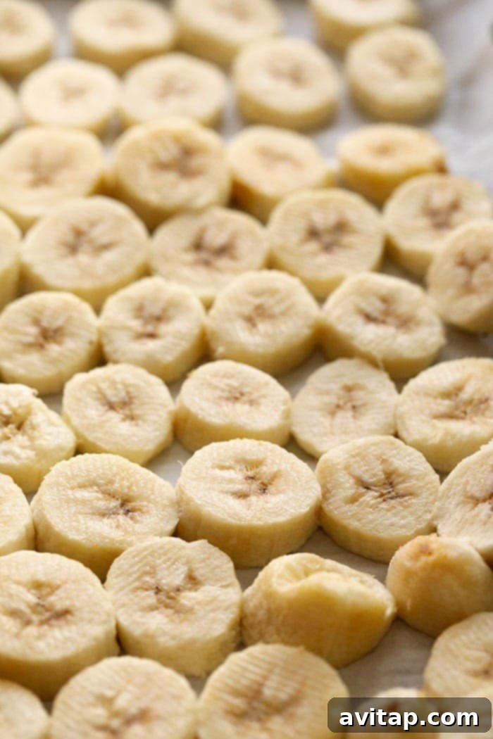 A close-up shot of perfectly flash-frozen banana slices on parchment paper, each piece distinct, firm, and ready for transfer to long-term storage