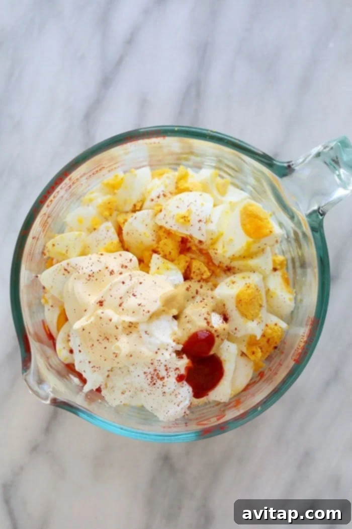 A Healthy Egg Salad recipe that packs a short list of whole ingredients and the delicious egg salad flavors you love. All the fresh and wholesome ingredients for healthy egg salad arranged in bowls, showcasing the simplicity and quality of the components: hard-boiled eggs, Greek yogurt, mayo, Dijon mustard, sriracha, and paprika.