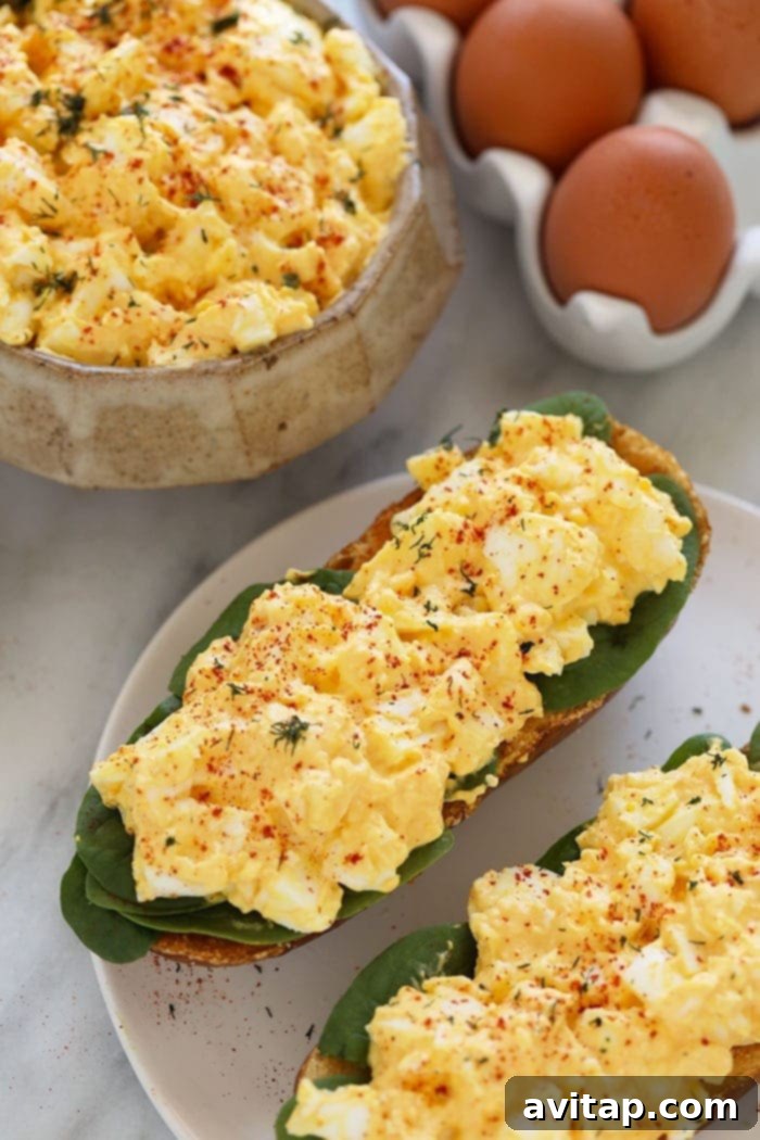 This healthy egg salad comes together with just 6 ingredients. It's a high-protein, low-carb salad that's enjoyable any day of the week. Two halves of healthy egg salad sandwiches arranged neatly on a plate, garnished with fresh herbs. The sandwiches highlight a delicious and easy way to enjoy this high-protein, low-carb recipe.