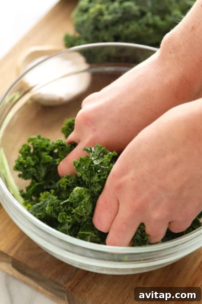 Close-up of two hands vigorously massaging kale in a large bowl, demonstrating the technique.