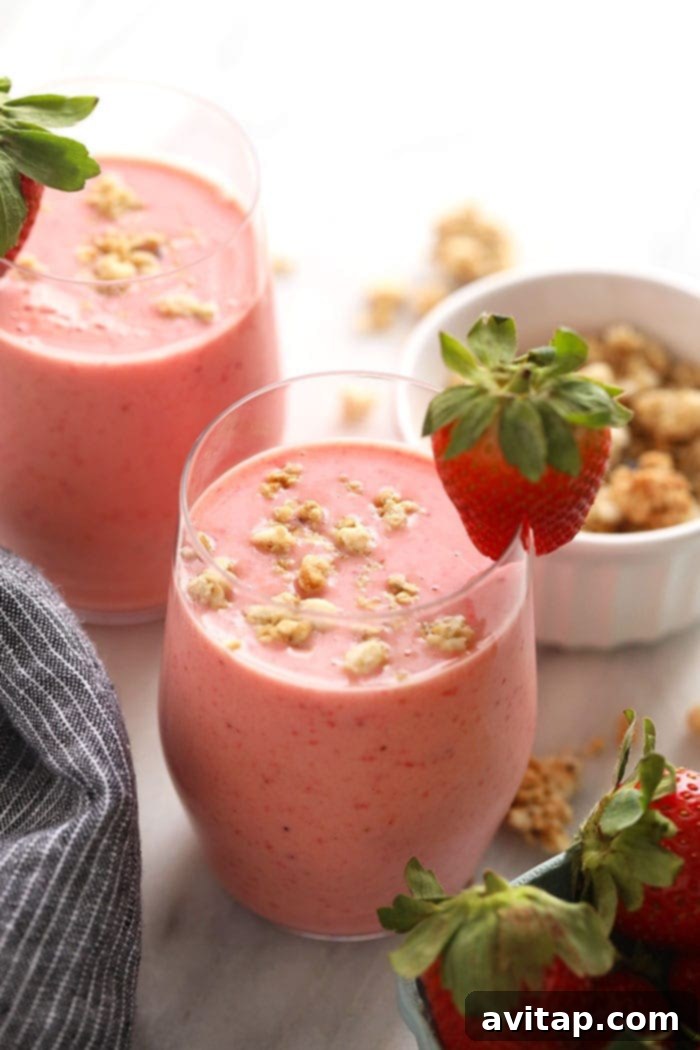A refreshing, creamy strawberry smoothie served in a clear glass, garnished with a fresh strawberry and mint leaf.