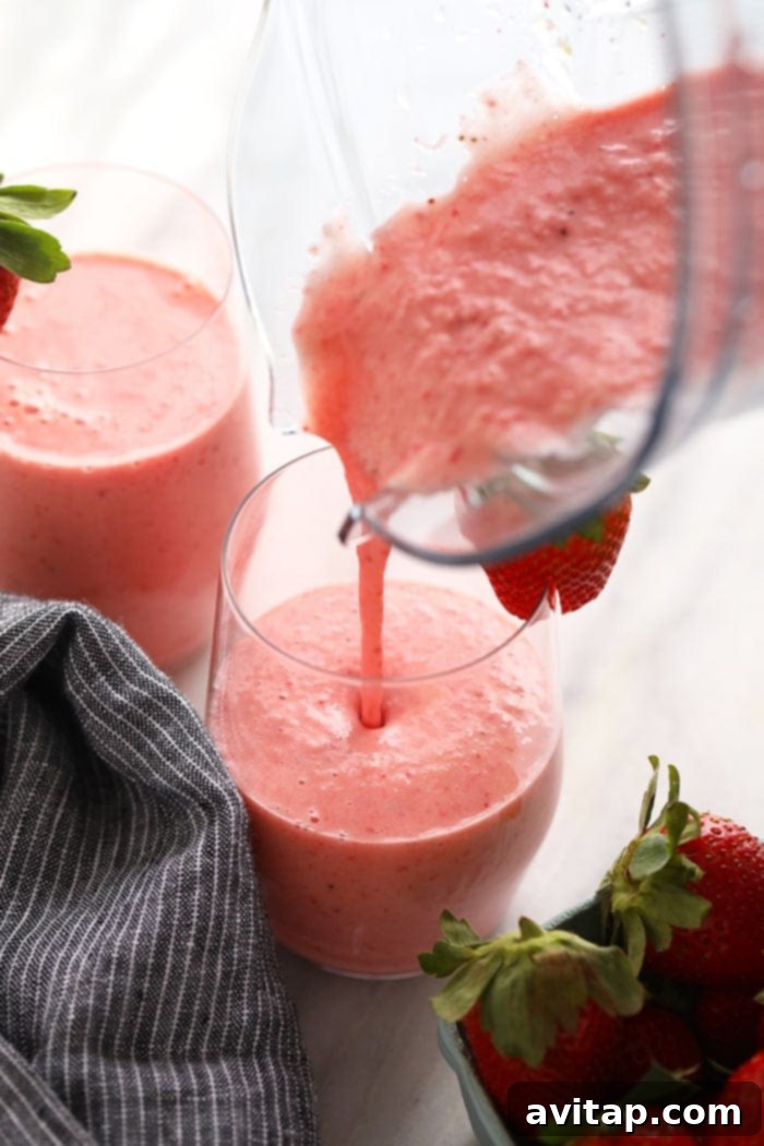 Thick, creamy strawberry smoothie being poured into a tall glass, showcasing its rich texture.