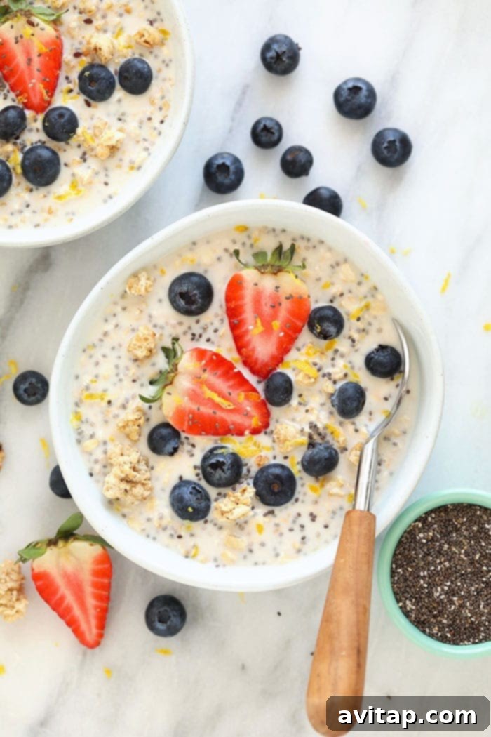 Overhead shot of a single serving of Lemon Cheesecake Overnight Oats, garnished with fresh berries and a slice of lemon.