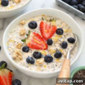 A bowl of creamy lemon cheesecake overnight oats, topped with fresh berries and a lemon slice.