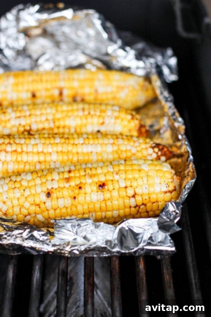 Foil-wrapped ears of Mexican street corn grilling over an open flame.