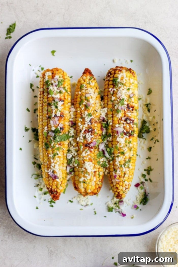 Freshly grilled Mexican street corn topped with cotija cheese, cilantro, and lime, served in a tin.