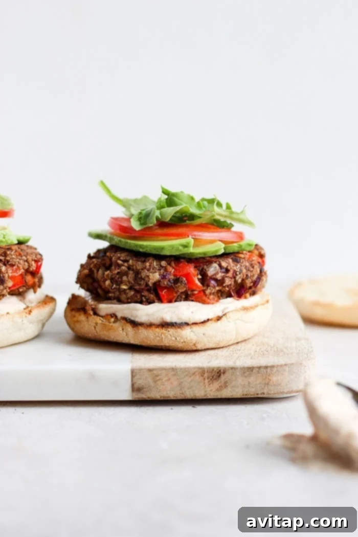 Ready-to-Eat Black Bean Quinoa Burger A fully assembled black bean quinoa burger on an English muffin with sauce, avocado, tomato, and arugula.