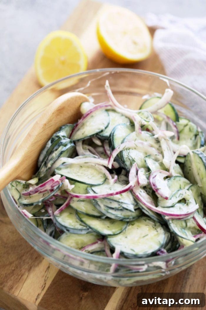 A large ceramic bowl filled with creamy cucumber salad, topped with fresh dill, ready to be served at a gathering. Highlighted as a healthy and flavorful addition to any meal.