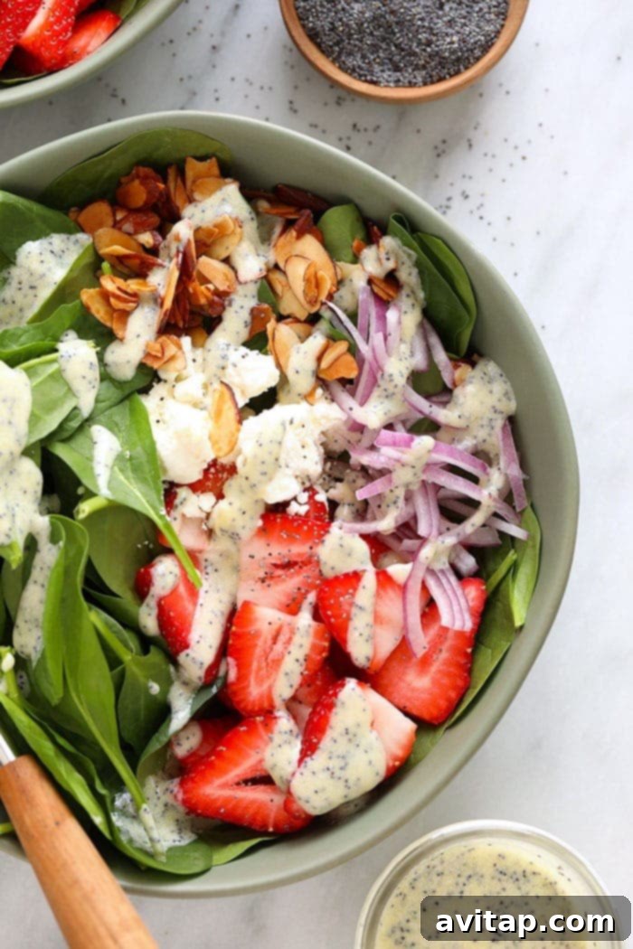 Close-up shot of a vibrant Strawberry Spinach Salad in a bowl, featuring tender spinach leaves, bright red strawberries, thinly sliced red onion, candied almonds, and a generous drizzle of creamy poppyseed dressing.