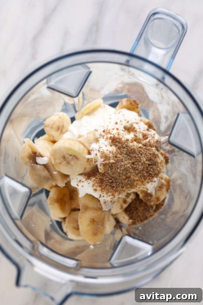 All the prepped ingredients for a healthy banana smoothie, including frozen banana slices, Greek yogurt, flax seeds, almond milk, and vanilla extract, carefully placed into a high-speed blender, ready to be blended into a creamy concoction.