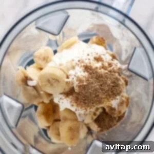 A high-speed blender filled with all the ingredients for a banana smoothie, ready for blending.