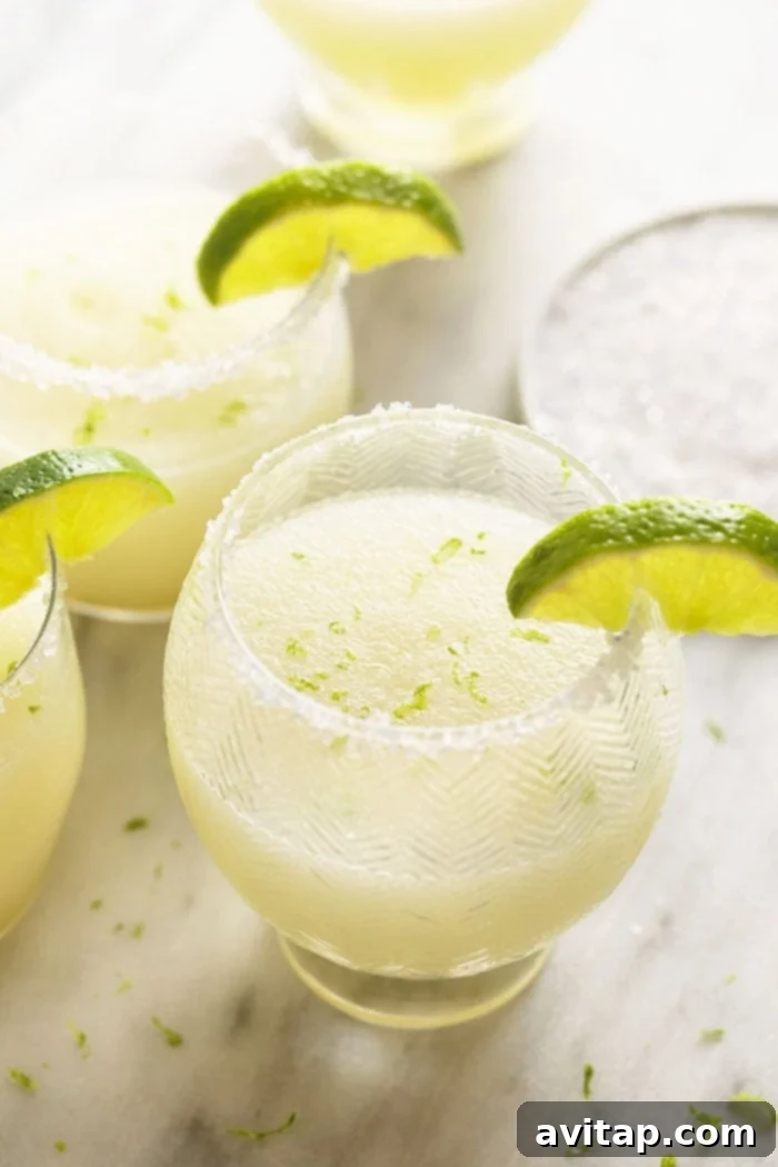 Two glasses of frozen margaritas garnished with lime wedges and salt rims, set against a vibrant background.