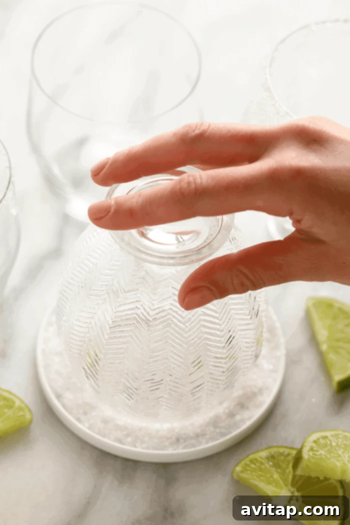 A hand dipping the rim of a margarita glass into a plate of coarse sea salt, ready for a frozen margarita.