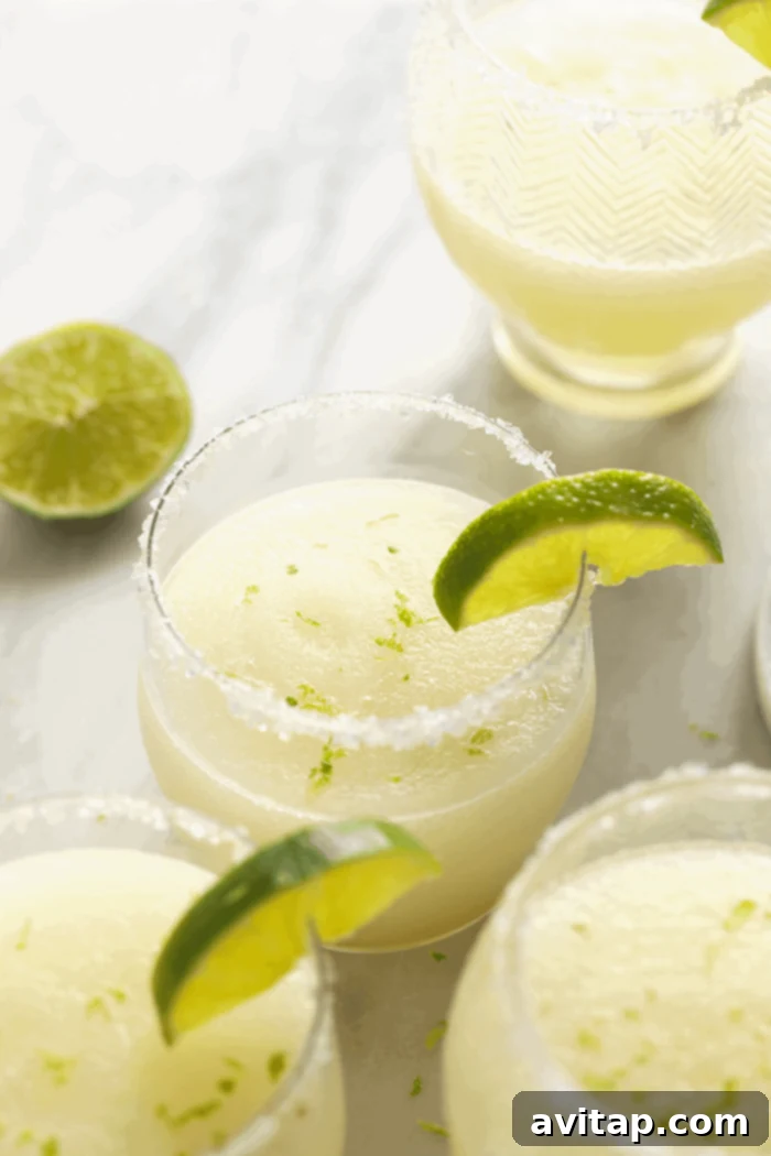A vibrant frozen margarita in a salt-rimmed glass, garnished with a fresh lime wedge, ready to be enjoyed.