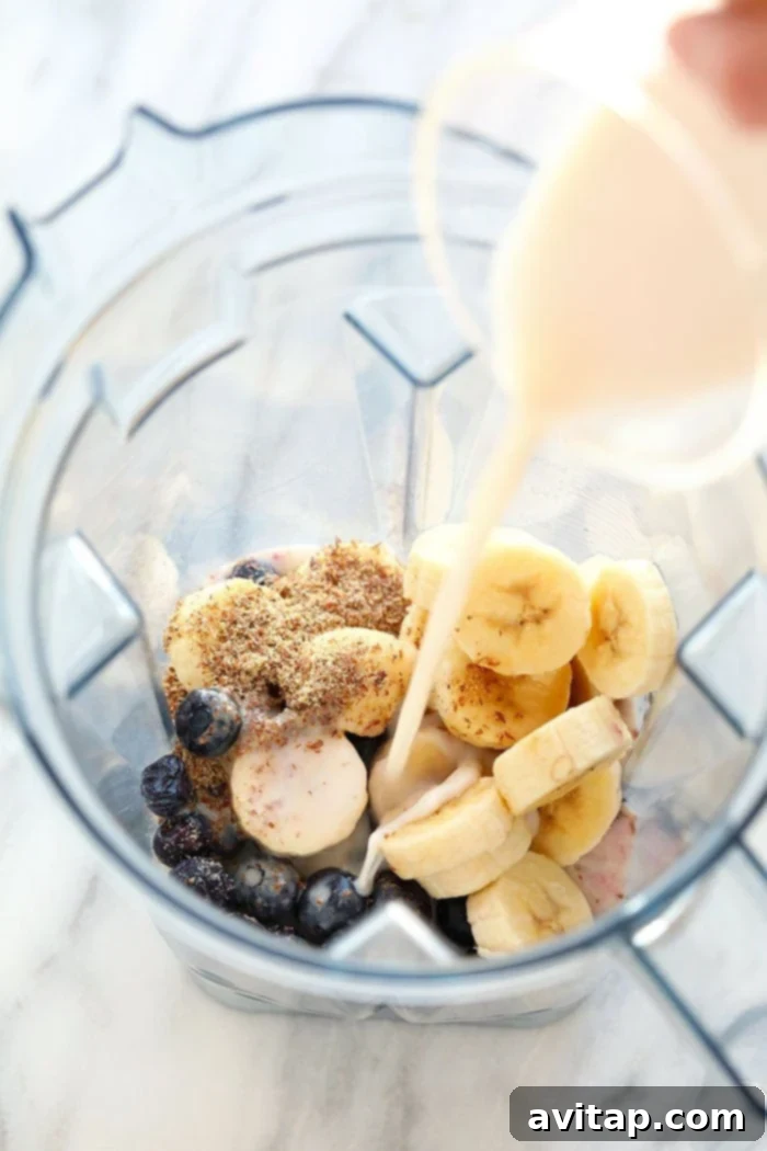 Preparing a healthy blueberry banana smoothie by adding almond milk to a blender. Almond milk being poured into a blender, with other smoothie ingredients waiting.