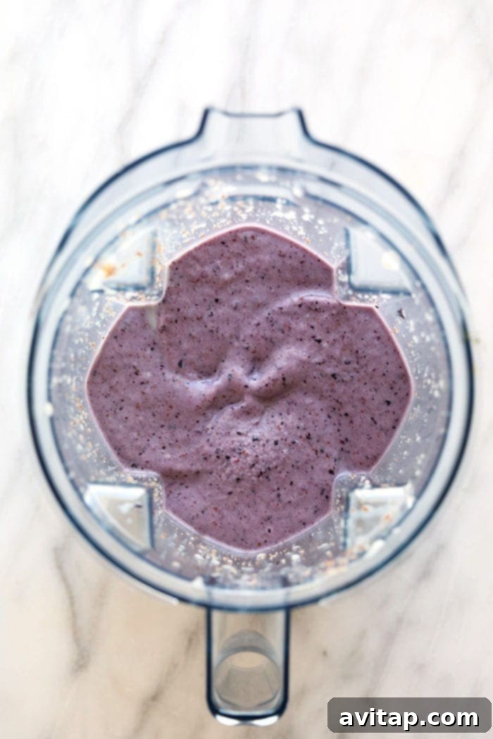 The vibrant blueberry banana smoothie blending to perfection in a high-speed blender. A blender filled with a thick, purple blueberry banana smoothie, ready to be poured.