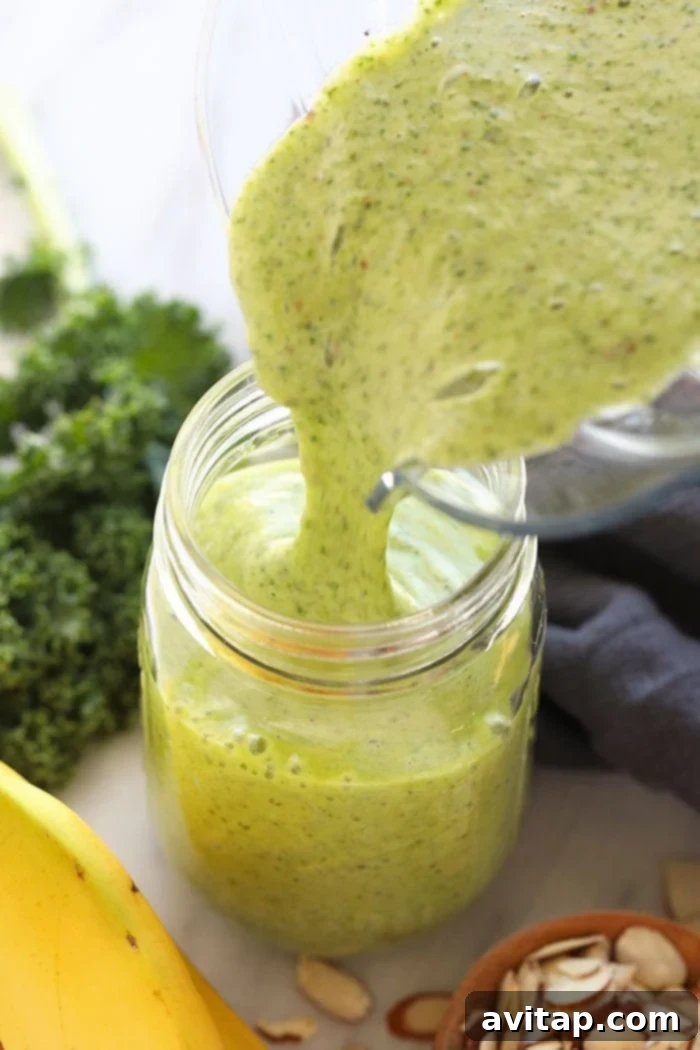 A vibrant green kale smoothie being poured from a high-speed blender into a stylish mason jar.