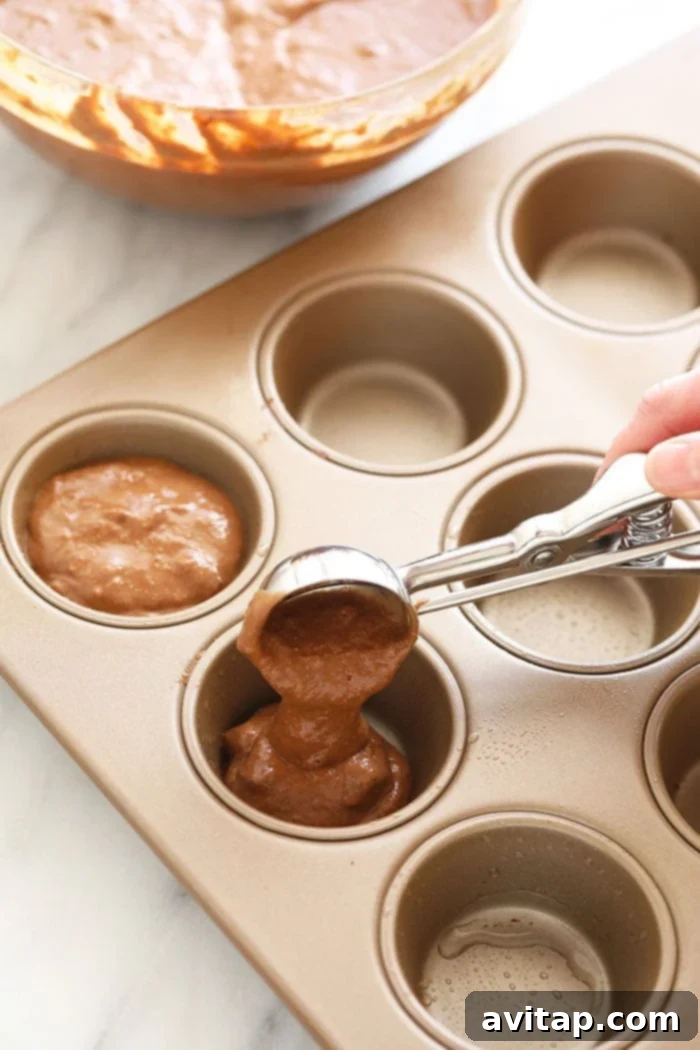 Scooping healthy chocolate muffin batter into a muffin tin, illustrating the preparation process.