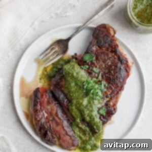 Sous vide steak on a plate, garnished with fresh green chimichurri sauce.