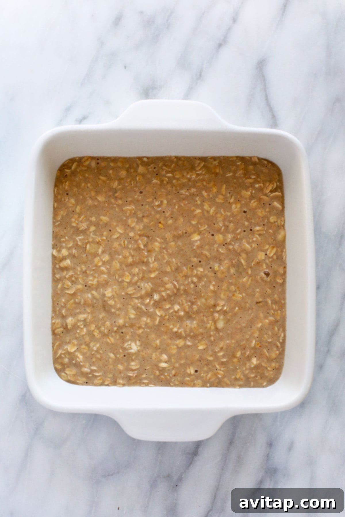 Close-up of baked oatmeal in a casserole dish, topped with various fruits and nuts, ready for serving.