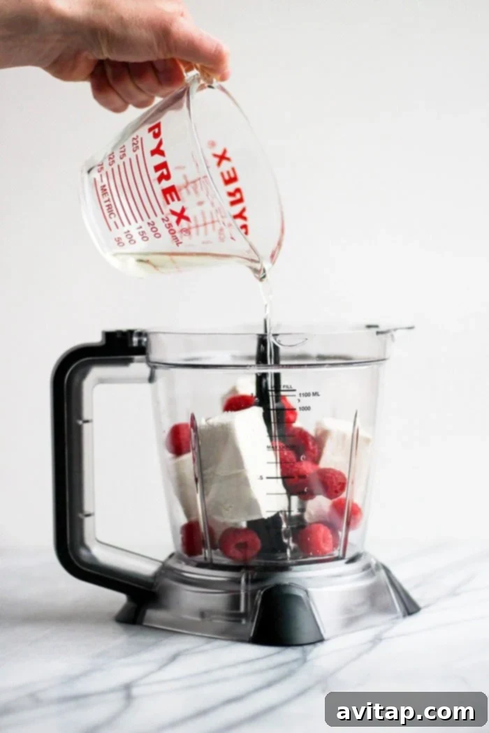 Pouring melted coconut oil into a food processor with other ingredients for fat bombs