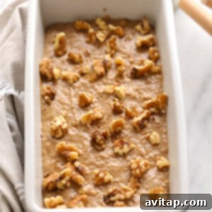 Vegan banana bread batter in a loaf pan, topped with chopped walnuts before baking.