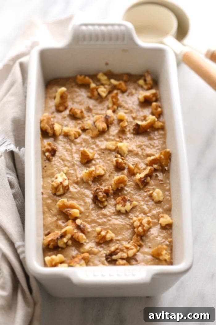 Vegan banana bread batter in a loaf pan, topped with walnuts before baking.