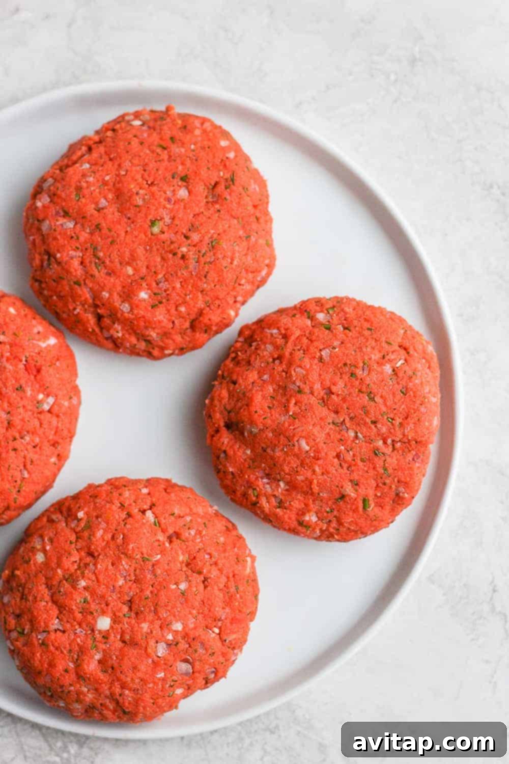 Raw salmon patties expertly formed and ready for cooking on a plate.